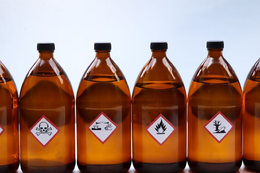 Flaschen stehen in einer Reihe. Auf den Flaschen sieht man verschiedene Warnsymbole. Per Klick gelangen Sie zur Seite Gefahrstoffe