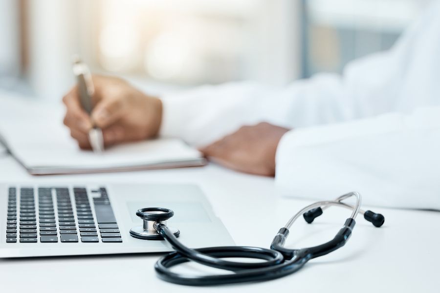 Laptop, Stethoskop und Arzt schreiben im Notizbuch. Per Klick gelangen SIe zu Seite des 
