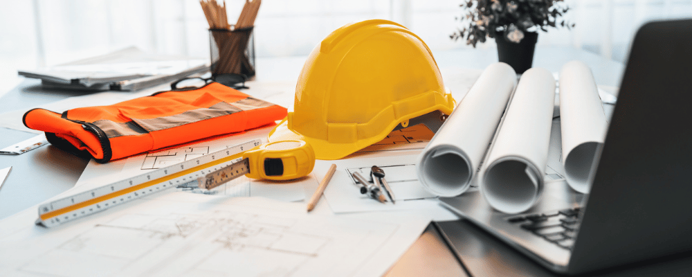 Arbeitsschutzhelm und zusammengerollte Pläne liegen auf einem Schreibtisch